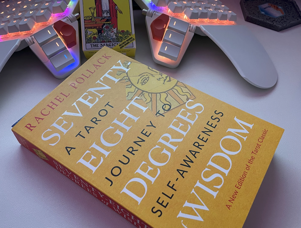 A photo of a book titled "Seventy-Eight Degrees of Wisdom" by Rachel Pollack is on a desk with a computer keyboard behind it.